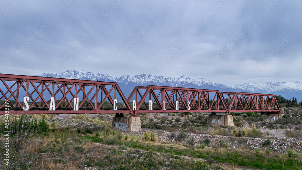 Vemos un viejo puente de ferrocarril , puro hierro forjado cruzando el rio Tunuyan , en el departamento de San Carlos provincia de Mendoza, de fondo la hermosa Cordillera de Los Andes. Vemos un viejo puente de ferrocarril , puro hierro forjado cruzando el rio Tunuyan , en el departamento de San Carlos provincia de Mendoza, de fondo la hermosa Cordillera de Los Andes.