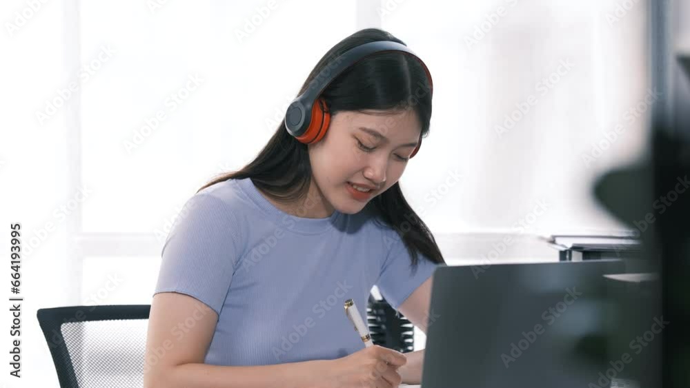 Young asian student woman taking notes while using laptop computer at home. Asian female learning online listening virtual video call. Business and education concept. Young asian student woman taking notes while using laptop computer at home. Asian female learning online listening virtual video call. Business and education concept.