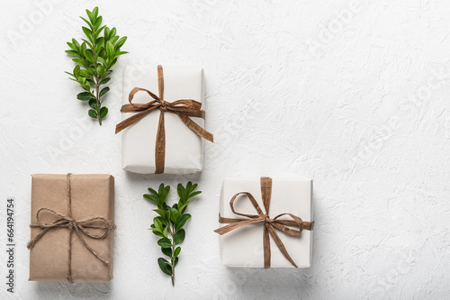 Three craft gift boxes on a white background and green boxwood branches. The concept of holidays and DIY gifts. Postcard, mock-up.