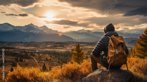 Back view of a man with a backpack sitting on a rock and looking at the landscape