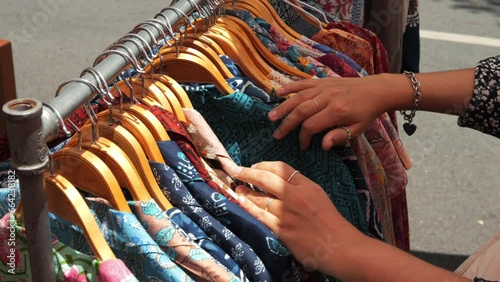 Young woman choosing a dress in a vintage boho second hand clothing store, female hands sort through clothes on a hanger. Chiang Mai, Northern Thailand. photo