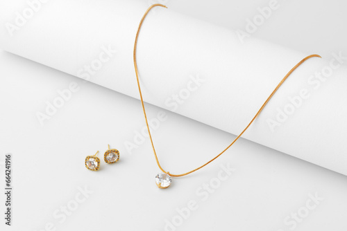 Golden necklace and diamond earrings on white paper background