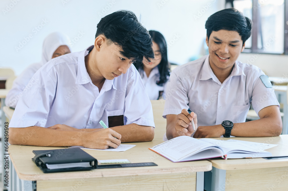 Young Asian students wear school uniform, sitting on desk in classroom and studying together Young Asian students wear school uniform, sitting on desk in classroom and studying together