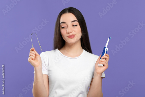 Woman with tongue cleaner and electric toothbrush on violet background