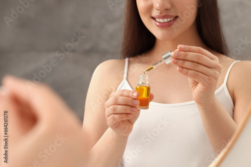 Woman with bottle of essential oil on blurred background, closeup