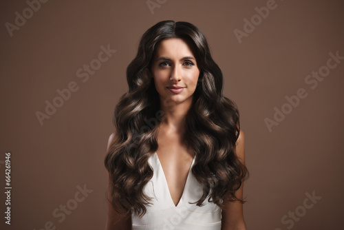 Gorgeous woman with shiny wavy hair on brown background. Professional hairstyling