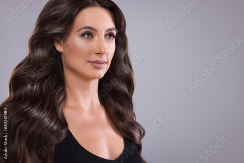 Gorgeous woman with shiny wavy hair on grey background, space for text. Professional hairstyling