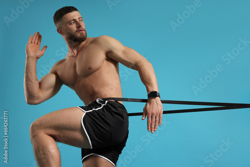 Muscular man exercising with elastic resistance band on light blue background
