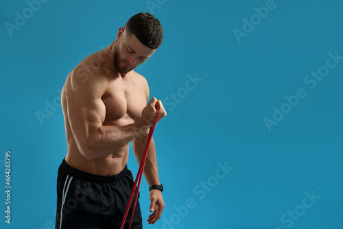 Tableau sur toile Muscular man exercising with elastic resistance band on light blue background