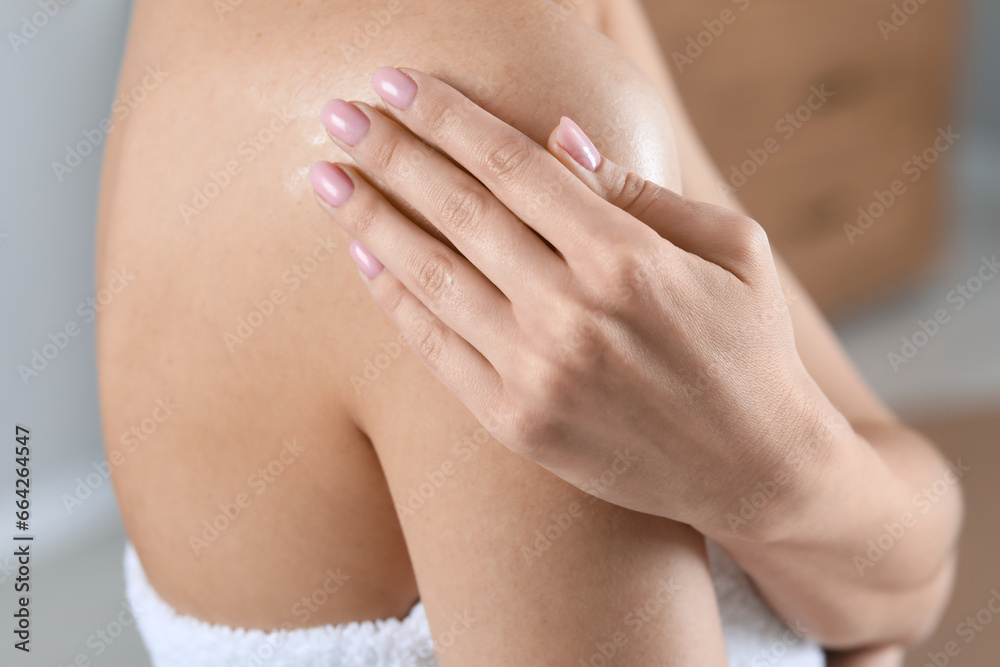 Woman applying body oil onto shoulder indoors, closeup