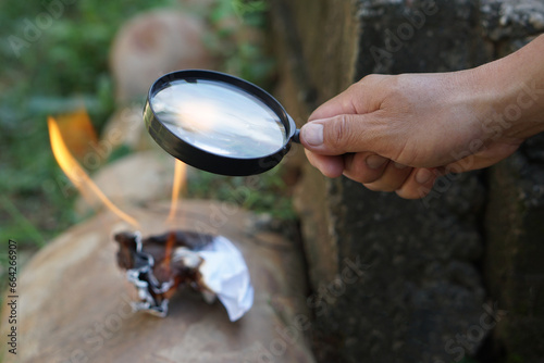 Close up hand hold magnifying glass to make fire for burning paper. Concept, Science experiment about convex lens, hold magnifying glass between the sun and tinder. Handy survival skills. 