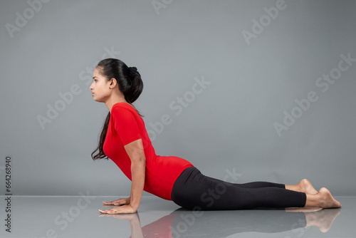 Healthy young woman in red t-shirt and black leggings doing yoga and stretching exercises isolated on grey background