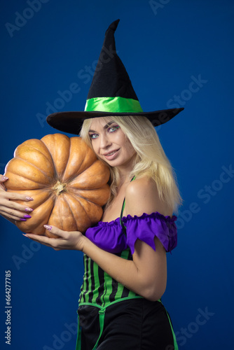 Blonde woman in a witch costume holding pumpkin in her hands