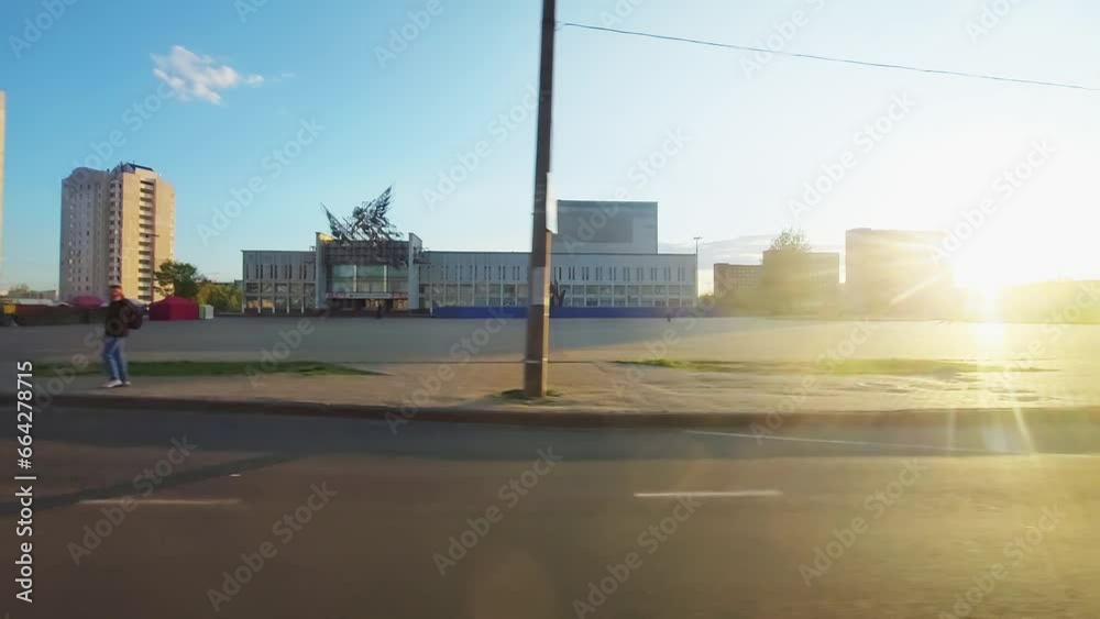 Overtaking passing of articulated bus. Road along high-rise residential buildings in the city. Background. View through side right car van wagon window on passenger seat in motion in town at sunset