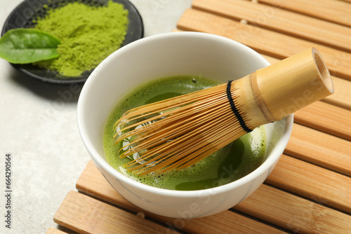 Cup of fresh matcha tea with bamboo whisk on light grey table, closeup