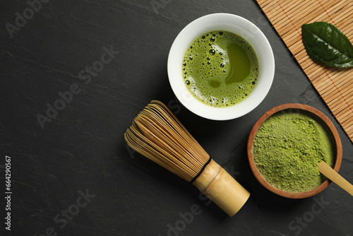 Cup of fresh matcha tea, green powder and bamboo whisk on black table, flat lay. Space for text