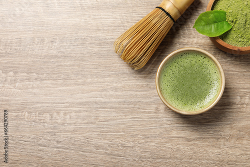 Cup of fresh matcha tea, bamboo whisk and green powder on wooden table, flat lay. Space for text