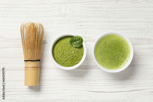 Cup of fresh matcha tea, bamboo whisk and green powder on white wooden table, flat lay