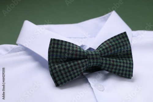 White shirt with stylish checkered bow tie on green background, closeup