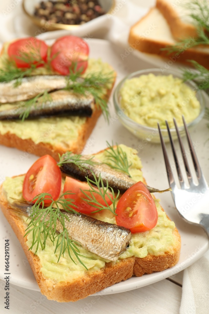 Delicious sandwiches with sprats, tomatoes, dill and avocado puree served on white wooden table Delicious sandwiches with sprats, tomatoes, dill and avocado puree served on white wooden table