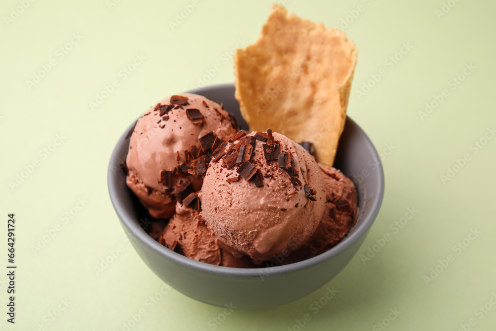 Tasty chocolate ice cream and piece of waffle cone in bowl on light green background, closeup Tasty chocolate ice cream and piece of waffle cone in bowl on light green background, closeup
