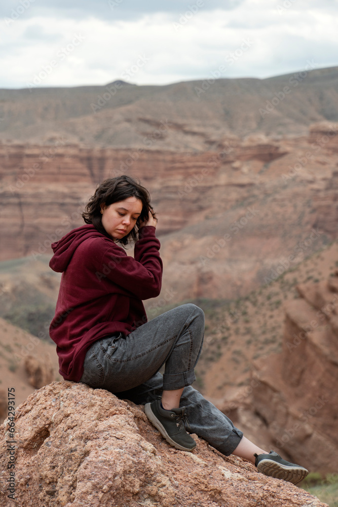 Naklejka premium A young woman sits on a rock in the Central Asian Canyon, Charyn, Kazakhstan