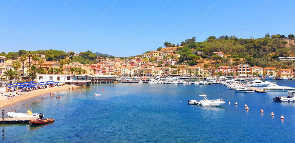Panorama of city Porto Azzuro with colorful houses and tourists on the beach.