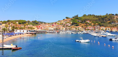 Panorama of city Porto Azzuro with colorful houses and tourists on the beach.