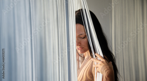 portrait of sensual seductive loving dreaming introverted sexy erotic nude woman standing by the window with thread curtain, casts body striped shadows