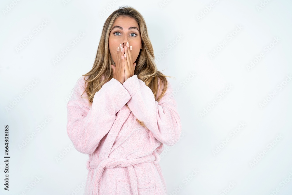 Funny Young caucasian woman wearing bathrobe keeps hands on mouth, looks with eyes full of disbelief, being puzzled with amount of work Funny Young caucasian woman wearing bathrobe keeps hands on mouth, looks with eyes full of disbelief, being puzzled with amount of work