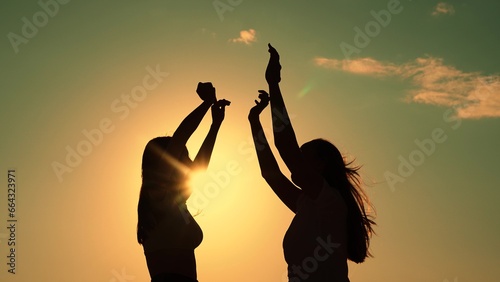 Friends have fun at beach party during sunset. Free girls dance merrily on summer evening, sun. Group of young people having fun dancing with raised hands to music. Celebrate summer day at beach party