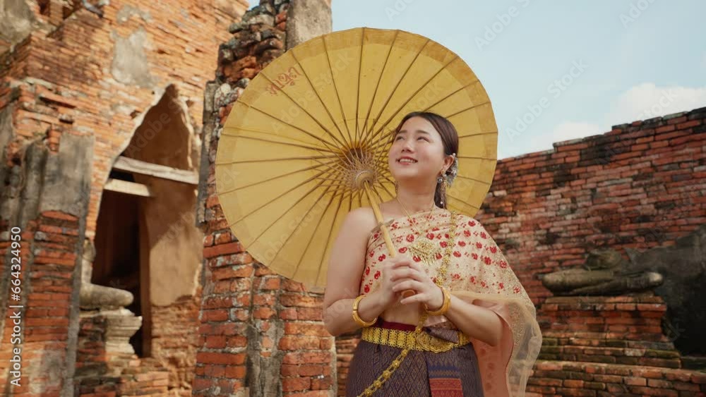 Young beautiful Asian woman wearing thai traditional dress holding umbrella in hand walking at ancient temple with old pagoda in Wat Chai Wattanaram Ayutthaya, Thailand