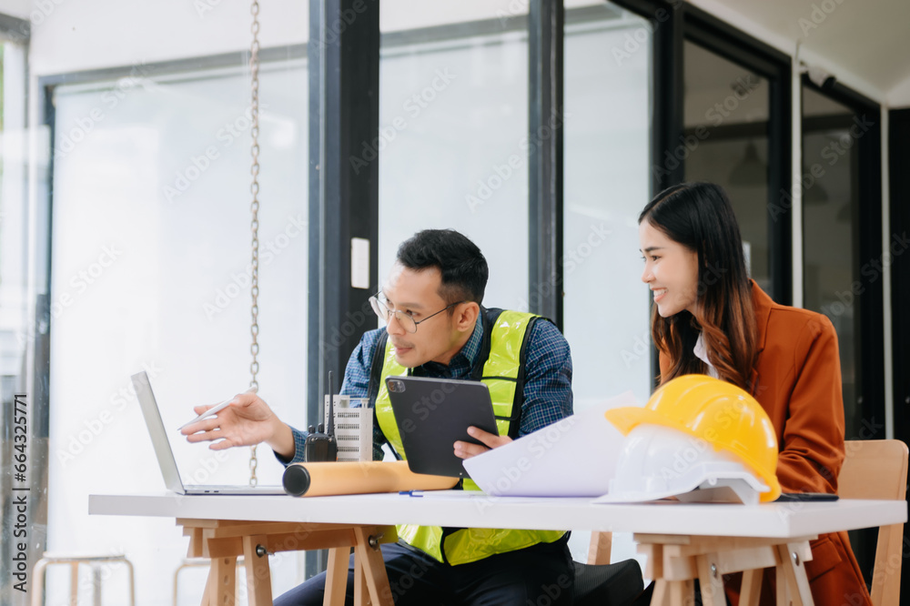 Two colleagues discussing data working and tablet, laptop with on architectural project at construction site at desk in office. Two colleagues discussing data working and tablet, laptop with on architectural project at construction site at desk in office.