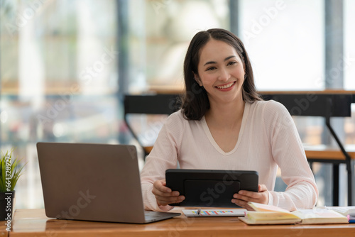 An Asian businesswoman using a digital tablet while sitting at a work desk in an office.