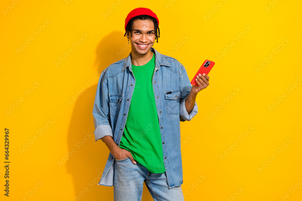Photo of nice positive man wear stylish denim shirt use modern device iphone samsumg isolated on bright yellow color background Photo of nice positive man wear stylish denim shirt use modern device iphone samsumg isolated on bright yellow color background