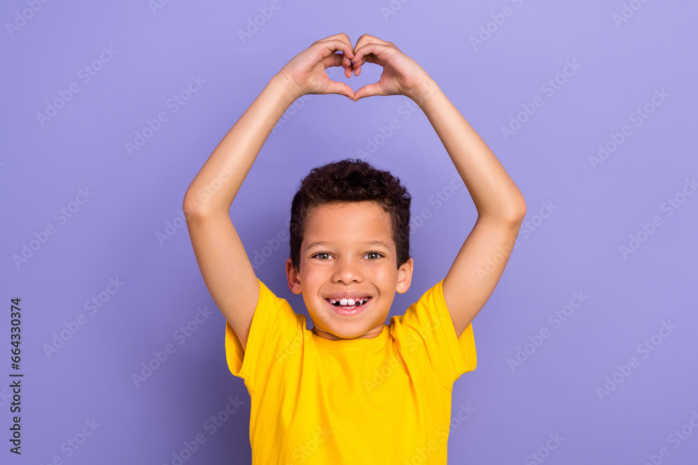 Photo of beautiful nice cheerful boy wear yellow trendy clothes showing you heart figure isolated on purple color background Photo of beautiful nice cheerful boy wear yellow trendy clothes showing you heart figure isolated on purple color background