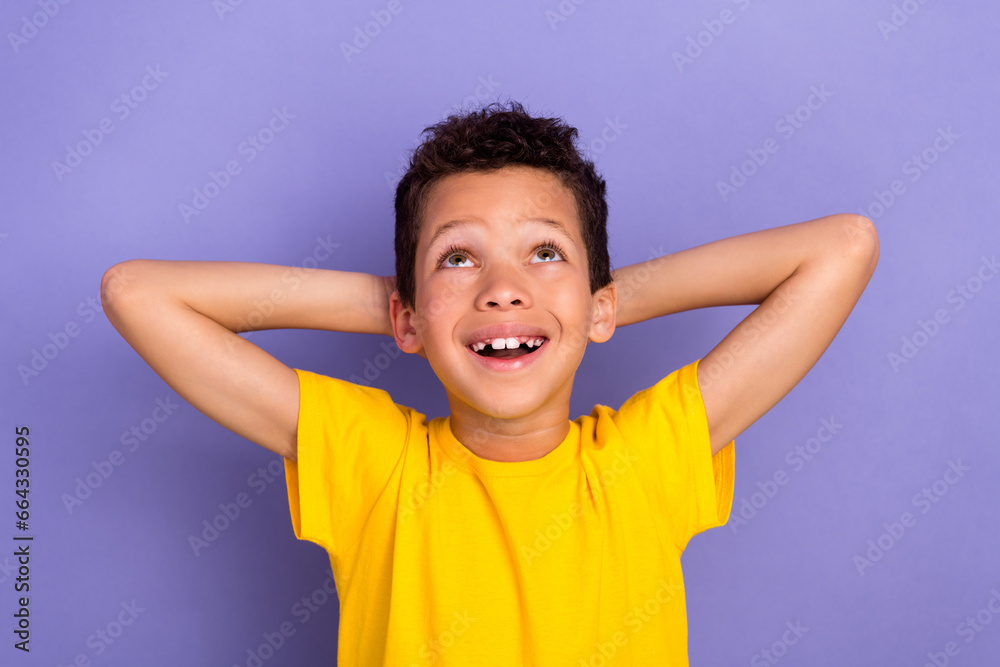 Photo of beautiful positive boy wear stylish clothes hold arms behind head look up empty space promo isolated on purple color background Photo of beautiful positive boy wear stylish clothes hold arms behind head look up empty space promo isolated on purple color background