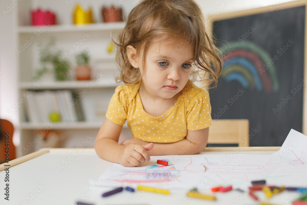 Young girl siting on the chair and drawing with colourful crayon. Home learning concept. Young girl siting on the chair and drawing with colourful crayon. Home learning concept.