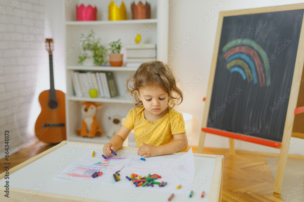 Fototapeta premium Young girl siting on the chair and drawing with colourful crayon. Home learning concept.