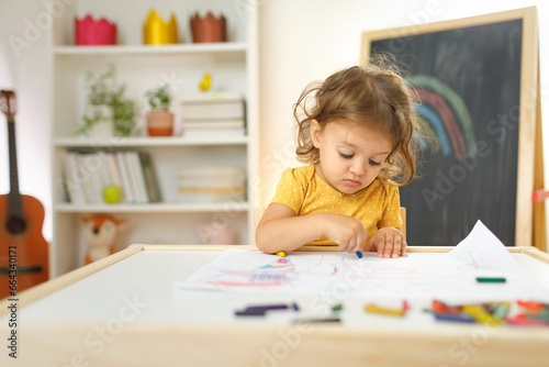 Young girl siting on the chair and drawing with colourful crayon. Home learning concept.