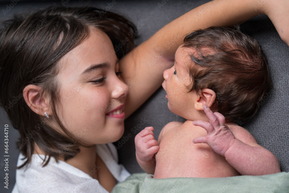 The older sister and her newborn younger brother are lying on the sofa. The girl looks at the baby with love. The kid took the hair in his hand. Family, love, newborn The older sister and her newborn younger brother are lying on the sofa. The girl looks at the baby with love. The kid took the hair in his hand. Family, love, newborn