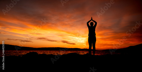 Kobieta ćwicząca joge na plaży na tle zachodu słońca, woman practicing yoga