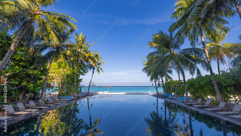 Popular tourism landscape. Luxury morning beach resort with swimming pool and beds chairs loungers under umbrellas with palm trees and blue sky reflections. Summer travel and best vacation background
