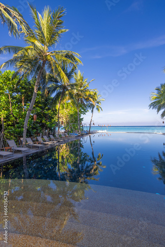 Fototapeta Naklejka Na Ścianę i Meble -  Popular tourism landscape. Luxury morning beach resort with swimming pool and beds chairs loungers under umbrellas with palm trees and blue sky reflections. Summer travel and best vacation background