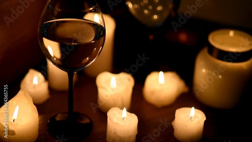 A glass of wine and candles in the dark. The focus shifts from the glass to the candles and the image is blurred in the side. Romantic dinner