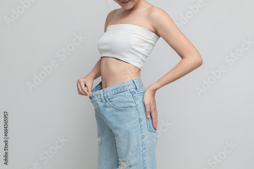 Happy  woman is showing her old oversized jeans after successful diet