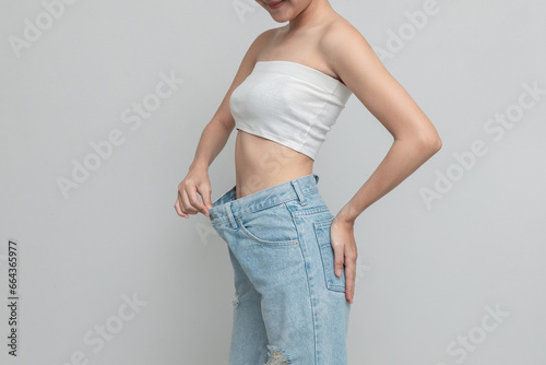 Diet concept for weight loss. A girl showing her old jeans after a successful diet. Woman in oversized jeans on a white background