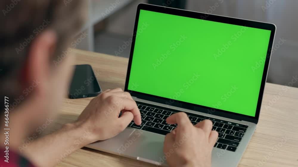 Young Man Uses Laptop With Green Mock-up Screen for Work or Study in Cozy Home Office. Chroma Key on Notebook Display Young Man Uses Laptop With Green Mock-up Screen for Work or Study in Cozy Home Office. Chroma Key on Notebook Display
