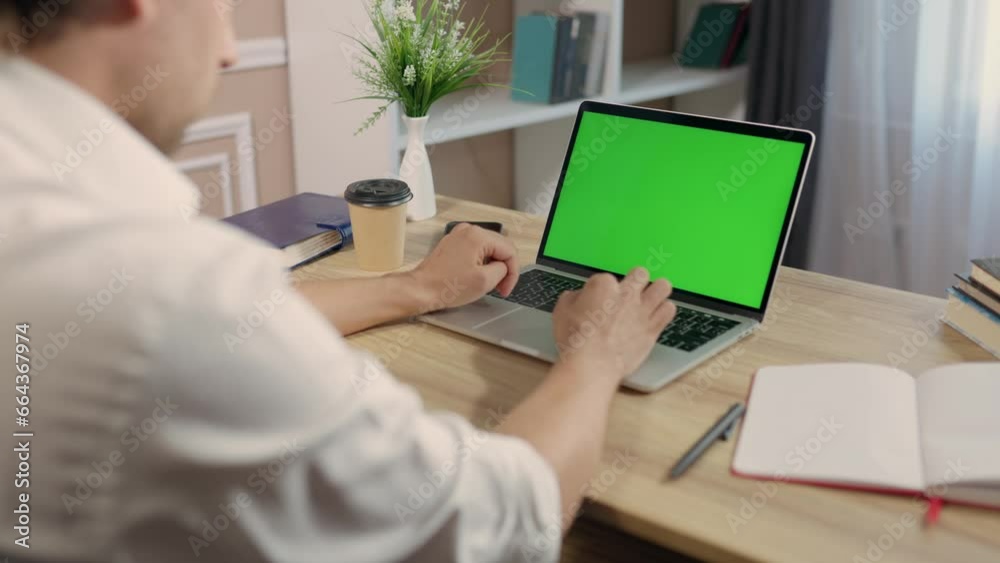 Young Man Uses Laptop With Green Mock-up Screen for Work or Study in Cozy Home Office. Chroma Key on Notebook Display Young Man Uses Laptop With Green Mock-up Screen for Work or Study in Cozy Home Office. Chroma Key on Notebook Display