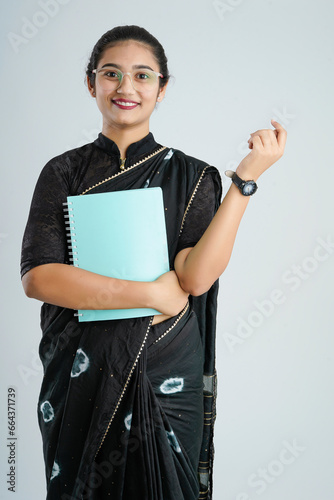 Portrait of Indian lady teacher in saree stands against white or blackboard , conducting online class using Camera, internet and lights